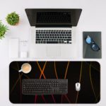 Golden curved lines crisscrossing on a black background, create a dynamic and elegant abstract design. Desk Mat with an Apple Laptop