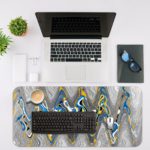 Infidu Artistic Desk Pad with a fluid, wavy pattern in blue, white, yellow, and gray, covering the entire surface. Desk Mat with an Apple Laptop