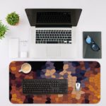 Desk mat featuring an abstract mosaic pattern with irregular shapes in shades of black, blue, gray, and yellow. Desk Mat with an Apple Laptop