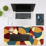 Infidu Artistic Patterns Desk Pad with overlapping curved shapes in maroon, beige, teal, and brown. Desk Mat with an Apple Laptop