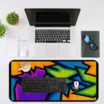 Infidu Artistic Patterns Desk Mat with sharp, angular shapes in purple, blue, green, orange, and black resembling graffiti. Desk Mat with an Apple Laptop