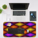 Infidu Artistic Patterns Desk Mat with 3D overlapping diamond shapes in gradient shades of purple, orange, and yellow. Desk Mat with an Apple Laptop