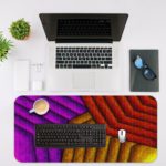 Infidu Artistic Patterns Desk Pad with a geometric zigzag pattern in warm hues of red, purple, and yellow, featuring a textured look. Desk Mat with an Apple Laptop