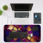 Infidu Artistic Patterns Desk Pad features a vibrant spiral design with rich colors including deep reds, oranges, yellows, purples, and blues. Desk Mat with an Apple Laptop