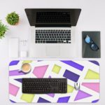 Infidu Artistic Desk Pad with geometric design in pastel pink, purple, blue, and yellow on a light background. Desk Mat with an Apple Laptop