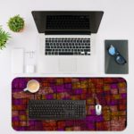 Infidu Artistic Patterns Desk Mat with a dark red and maroon background and a mosaic grid pattern in shades of orange, brown, and yellow. Desk Mat with an Apple Laptop