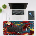 Infidu Artistic Patterns Desk Pad features a colorful abstract design with blue, red, yellow, and black layered shapes and lines. Desk Mat with an Apple laptop