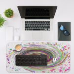 Infidu Artistic Desk Pad with a rainbow spiral and multicolored splatter on a white background. Desk Mat with an Apple Laptop