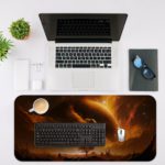 Infidu Space Desk Pad features a rocky planet with a dramatic sun against a swirling orange and yellow sky. Desk Mat with a laptop