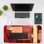 Infidu Artistic Desk Mat with an abstract composition of overlapping rectangular shapes in red, orange, and beige tones. Desk Mat with an Apple Laptop