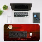 Infidu desk pad featuring a small boat on a red ocean under a red sky, capturing a serene sunrise or sunset scene. Desk Mat with an Apple Laptop