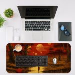 Desk pad featuring a colorful sunset over a forest, with warm shades of red, orange, and yellow. Trees in the foreground and a glowing sun in the sky. Desk Mat with an Apple Laptop