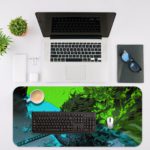 Desk pad featuring a vibrant nature scene with a blue river flowing through lush, green vegetation. Desk Mat with an Apple Laptop