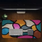 Infidu Artistic Desk Mat with organic, curving multicolored shapes in pink, light blue, yellow, gray, and white. Desk Pad in computer table