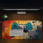 Gaming Desk Pad featuring a blue, red, and yellow controller with a sandal orange and yellow background, accented with vibrant paint splashes Desk Pad with Antique Video Game Design Kept on a computer table