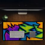 Infidu Artistic Patterns Desk Mat with sharp, angular shapes in purple, blue, green, orange, and black resembling graffiti. Desk Pad in computer table