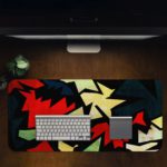 Infidu Artistic Patterns Desk Pad with sharp, jagged shapes in a zigzag design featuring bold colors like red, white, green, and black. Desk Pad on computer table