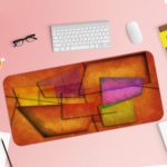 Infidu Artistic Desk Mat with abstract rectangular and trapezoidal shapes in warm tones of orange, red, purple, and yellow. Desk Pad with Keyboard and Mouse