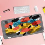 Infidu Artistic Patterns Desk Pad with bold, brushstroke-like shapes in yellow, black, red, and white on a gray background. Desk Pad with Keyboard and Mouse