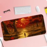 Desk pad featuring a colorful sunset over a forest, with warm shades of red, orange, and yellow. Trees in the foreground and a glowing sun in the sky. Desk Pad with Keyboard and Mouse