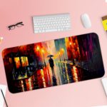 Desk pad featuring a vibrant nighttime city scene with bright colors reflecting off wet streets. Silhouette of a person with an umbrella in the center. Desk Pad with Keyboard and Mouse