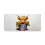 Desk pad with a fluffy brown highland cow sitting in a blue and white bucket, surrounded by yellow flowers and greenery on a light grey background. Desk Pad kept on a plain white background