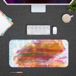 Infidu Artistic Desk Pad with pastel brushstroke patterns in light blue, white, pink, and orange. Design Kept on a computer table