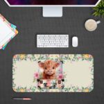 Desk pad with a playful cow design, yellow rose, and pink and white flowers in the background. Desk Pad kept on a plain gray background