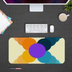 Infidu Artistic Desk Mat with a circular pattern in overlapping shades of yellow, orange, purple, and blue. Design Kept on a computer table