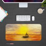 Desk mat featuring a sunset scene with a silhouette of a sailboat on an orange-gold sea, under a warm yellow and golden sky. Design Kept on a computer table