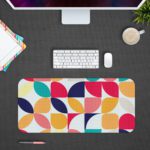 Infidu Artistic Desk Mat with a colorful geometric pattern of overlapping circles and quarter-circles in navy, pink, orange, teal, and yellow. Desk Pad with Design Kept on a computer table