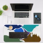 Infidu Artistic Desk Mat with an abstract landscape design in blue, white, green, and brown. Desk Mat with an Apple Laptop