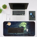 Godzilla rises over a city at night with a white moon and clouds on a desk mat. Desk Mat with an Apple Computer