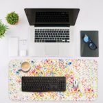 Infidu Artistic Desk Mat with speckled colorful dots in blue, red, yellow, and green on a white background. Desk Mat with an Apple Laptop