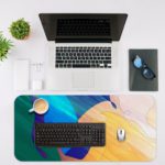 Infidu Artistic Desk Mat with flowing abstract shapes in blue, green, yellow, and orange. Desk Mat with an Apple Laptop