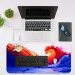 Bright orange and red curling wave against a deep blue background. Desk Mat with an Apple Laptop