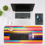 Infidu Artistic Desk Pad with horizontal stripes in pink, yellow, purple, blue, and red. Desk Mat with an Apple Laptop