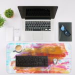 Infidu Artistic Desk Pad with pastel brushstroke patterns in light blue, white, pink, and orange. Desk Mat with an Apple Laptop