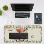 Desk pad with a playful cow design, yellow rose, and pink and white flowers in the background. Desk Mat with an Apple Computer