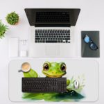 Desk pad with a green frog sitting on the grass and surrounded by leaves, set against a white background. Desk Mat with an Apple Computer