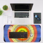 Infidu Artistic Desk Mat with circular pattern and concentric rings in orange, yellow, blue, and green. Desk Mat with an Apple Laptop