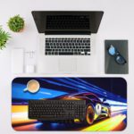 Desk pad featuring a stylized sports car in motion with blue, yellow, and orange light trails. Desk Mat with an Apple Laptop