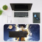 Japanese anime character with spiky dark hair in a yellow outfit, powering up against a blue, rainy background on a desk pad. Desk Mat with an Apple Laptop