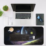 Infidu Space Desk Mat featuring multiple planets and a spacecraft against a deep space background with stars, in shades of blue and green. Desk Mat with a laptop