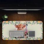 Desk pad with a playful cow design, yellow rose, and pink and white flowers in the background. Desk Pad on the computer table