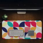 Infidu Artistic Desk Mat with a colorful geometric pattern of overlapping circles and quarter-circles in navy, pink, orange, teal, and yellow. Desk Pad in computer table