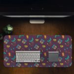 Infidu Creative Gaming Joystick Pattern Desk Pad featuring a dark maroon background with colorful illustrations of game controllers, headphones, and cassette tapes Game Design Kept on a computer table