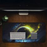 Infidu Space Desk Mat features a large glowing planet or star against a dark space background with swirling yellow-green gases. Desk Mat with a computer