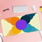 Infidu Artistic Desk Mat with a circular pattern in overlapping shades of yellow, orange, purple, and blue. Desk Pad with Keyboard and Mouse