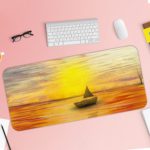 Desk mat featuring a sunset scene with a silhouette of a sailboat on an orange-gold sea, under a warm yellow and golden sky. Desk Pad with Keyboard and Mouse